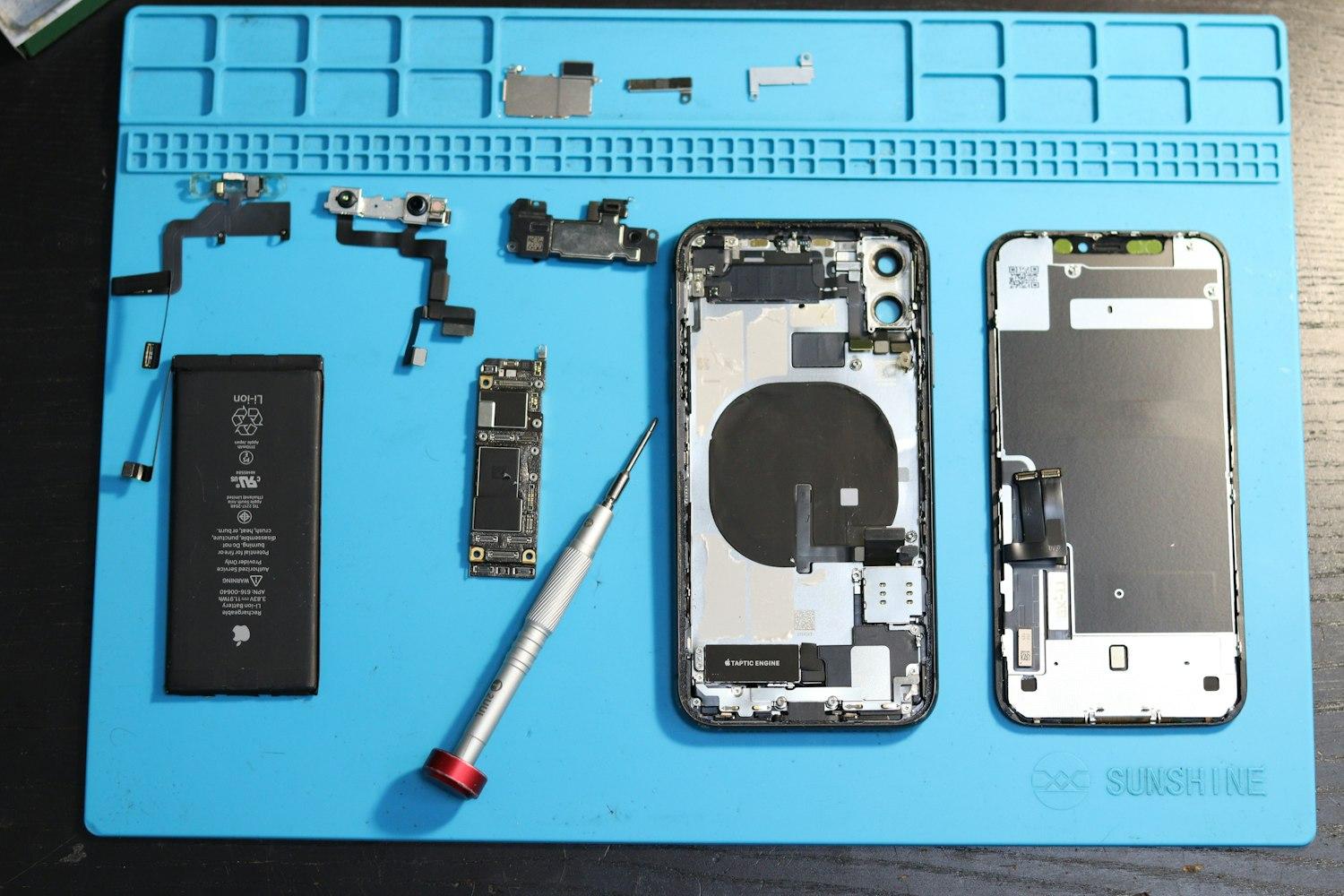 Zerlegtes Smartphone mit Akku, Platine und Displayeinheit auf einer blauen Reparaturmatte